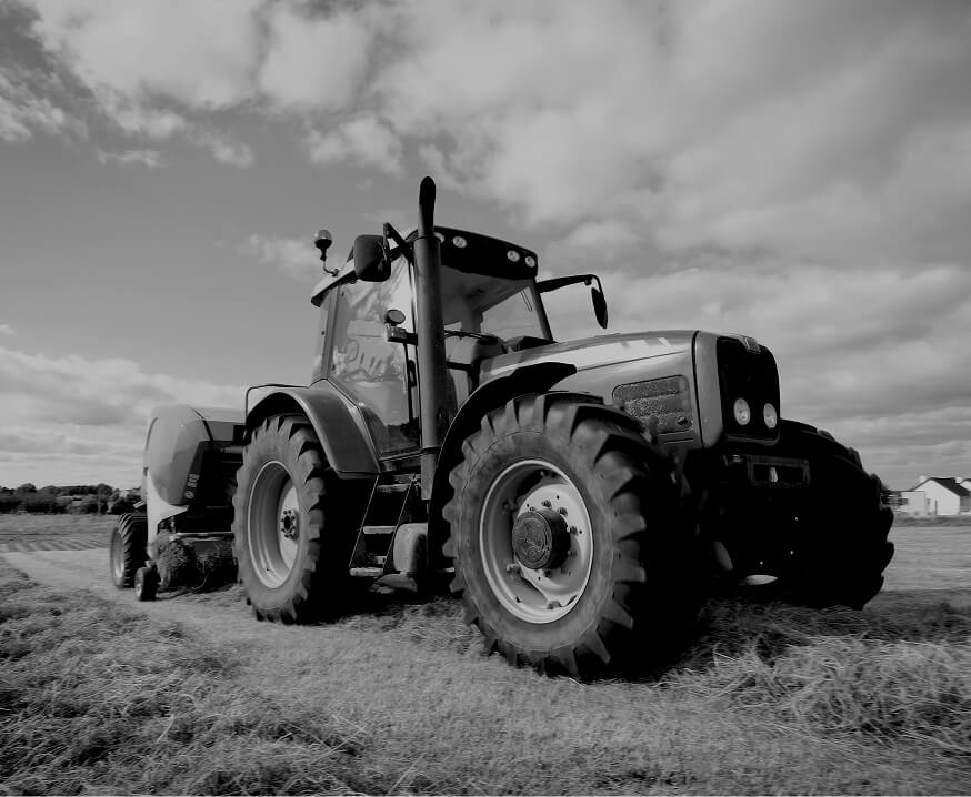 Large agricultural tractor with baler attachment working in a field, representing precision machined components for farming equipment