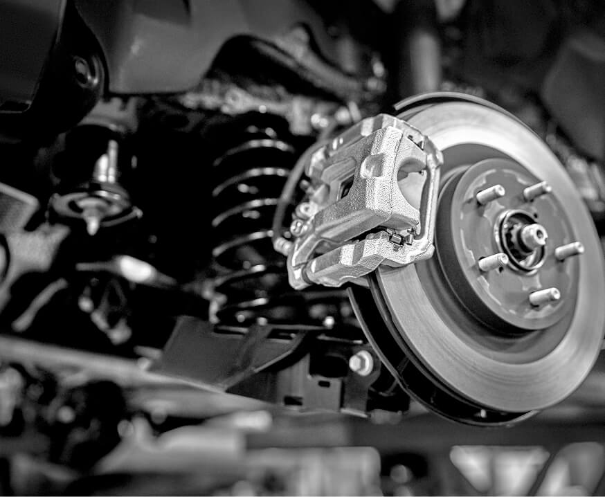 Automotive brake caliper and rotor assembly on vehicle suspension, representing precision machined brake and drivetrain components for the automotive industry