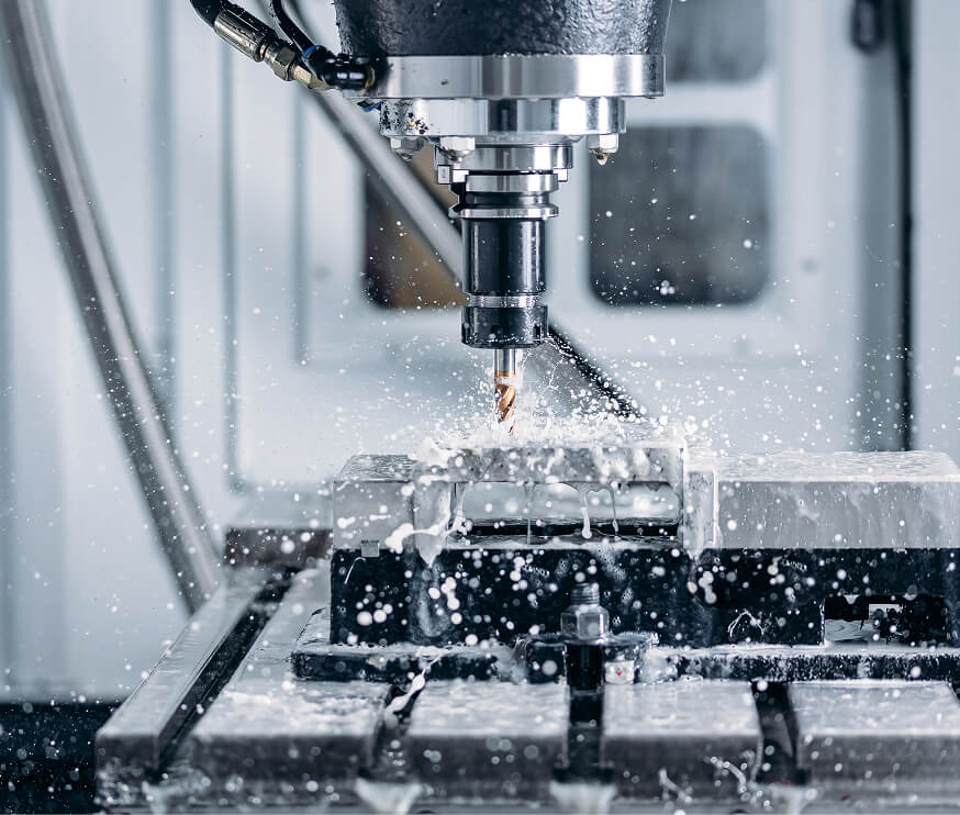CNC milling operation with carbide drill bit cutting into a steel workpiece with flood coolant spray on a precision machining center
