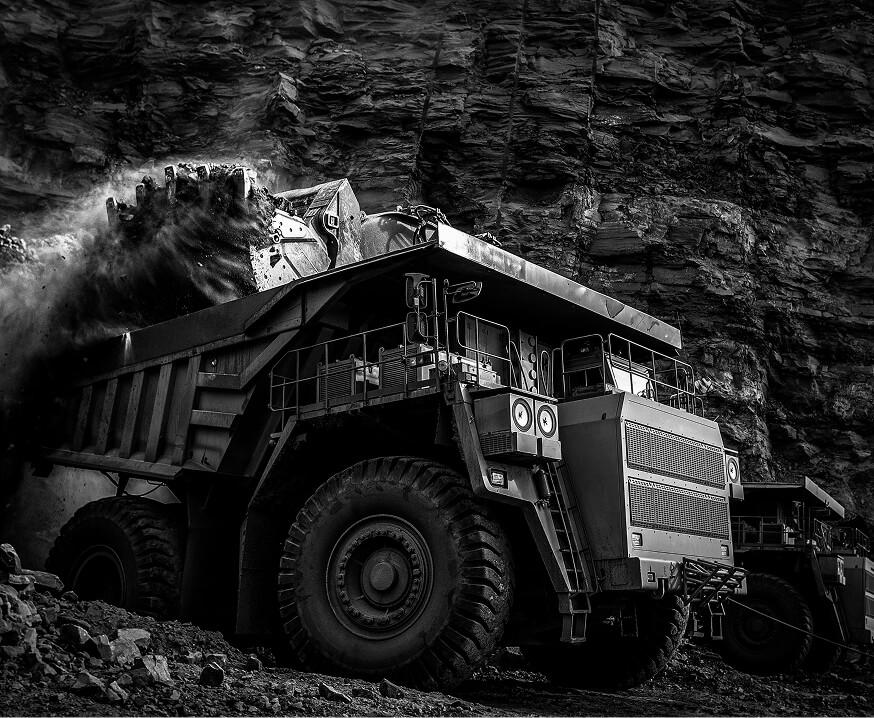 Heavy-duty mining haul truck being loaded with ore in an open pit mine, representing precision machined components for mining and heavy equipment