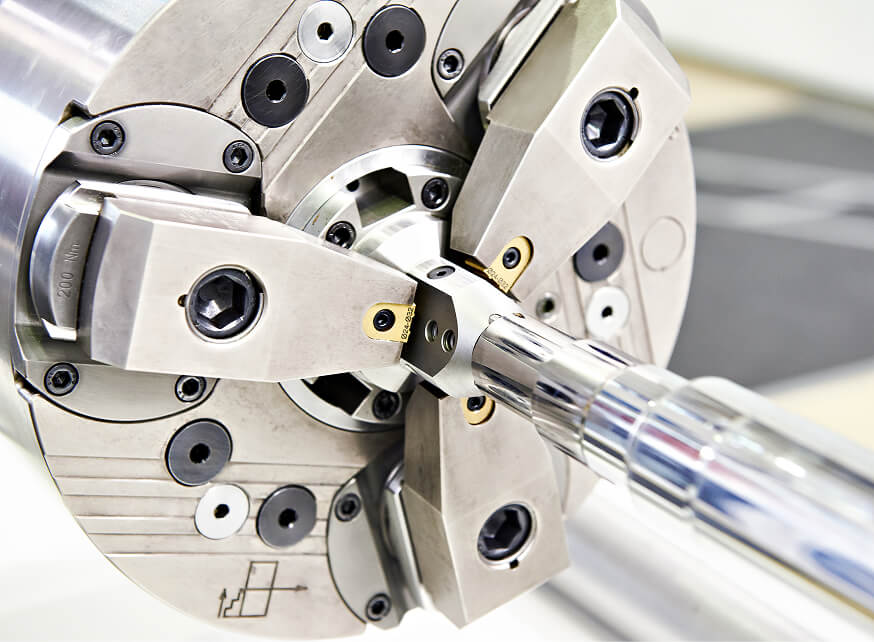 CNC turning operation with carbide insert tooling cutting a precision-ground steel shaft on a multi-jaw lathe chuck